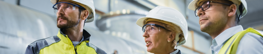 Three Heavy Industry Engineers Stand in Pipe Manufacturing Factory, Use Digital Tablet Computer, Have Discussion. Large Pipe Assembled